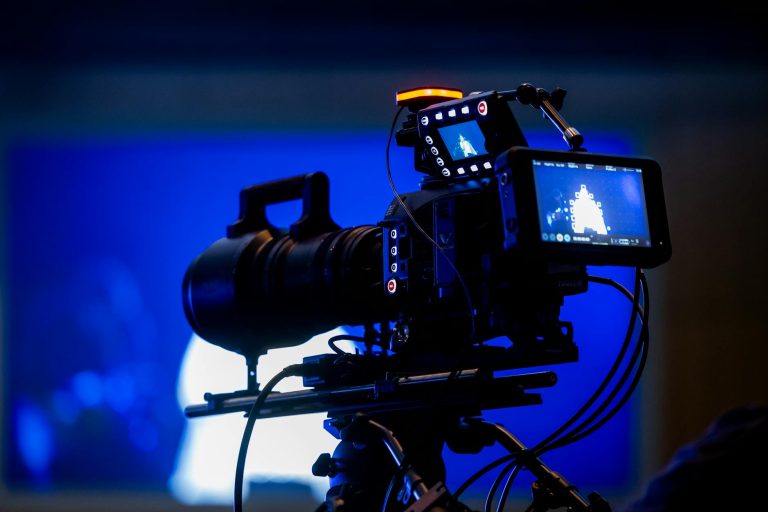 High-end video camera rig in studio setting with auxiliary monitor displays and vibrant blue lighting.